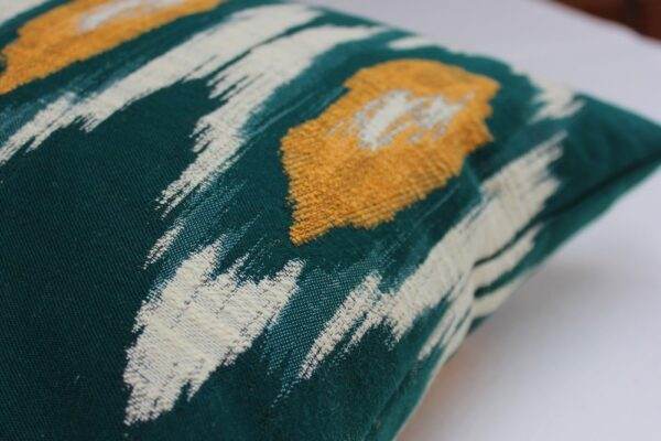 A green and yellow pillow with a Mind the Gap - Ikat, Green & Orange pattern.