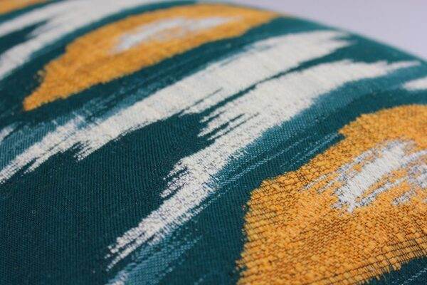 A close up of a Mind the Gap - Ikat, Green & Orange pillow with yellow and green designs.