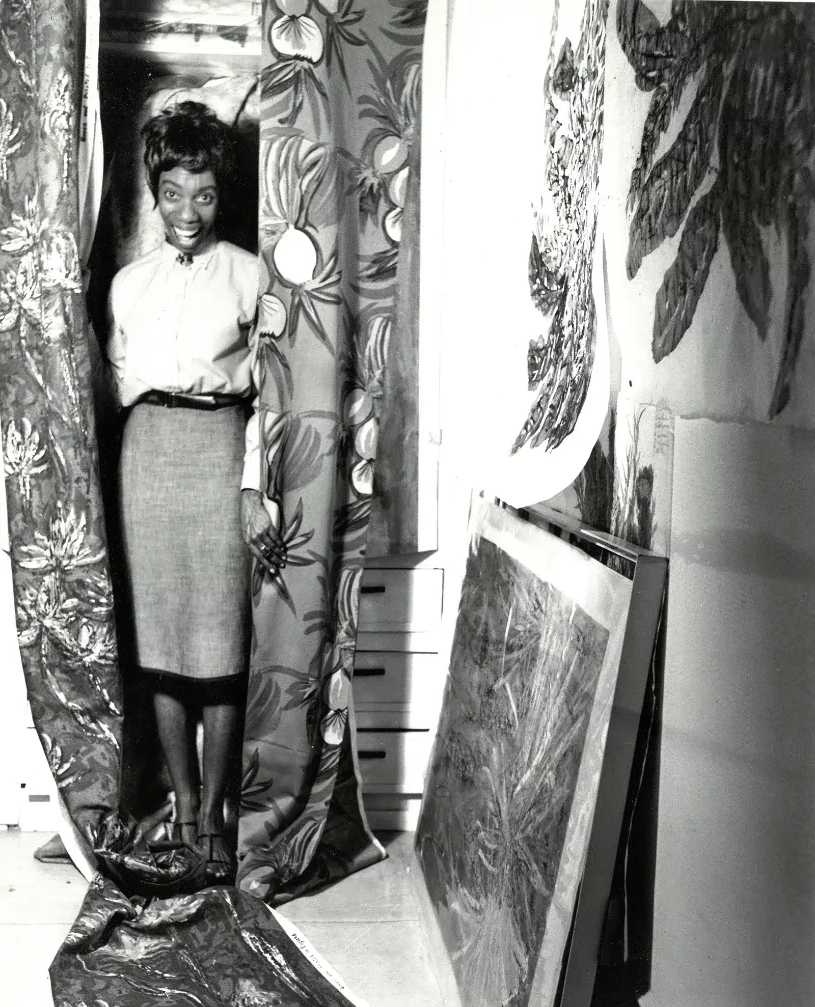 A black and white photo of a woman standing in front of a curtain.