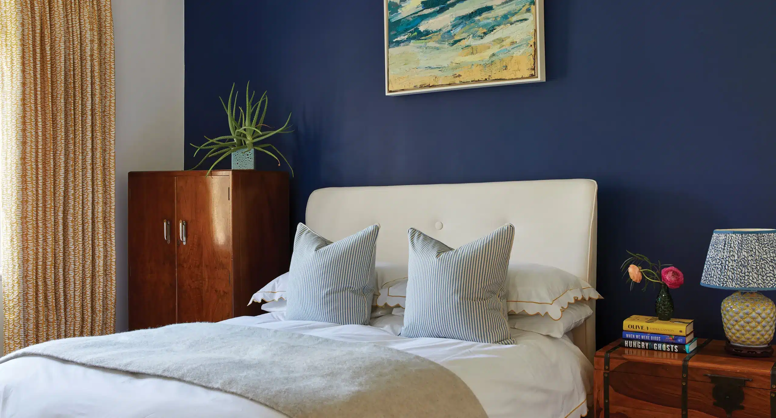 A bedroom with blue walls and white furniture is enhanced by custom-made curtains and blinds.